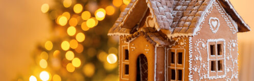 gingerbread house over defocused lights of Chrismtas decorated fir tree. Christmas eve, warm atmospheric light
