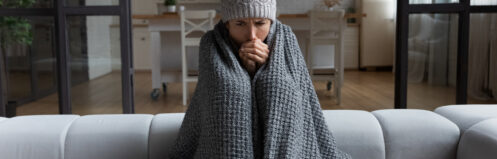 Cold woman sitting on couch while wrapped up in blankets